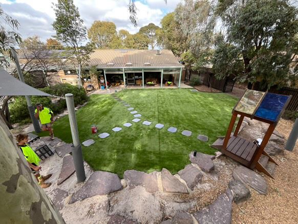 Nature play kindergarten yard with synthetic turf, stepping stone path, rock work and shade sails, built by Sunnybank Horticultural
